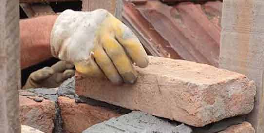 Masonry Repair Service - Photo of a man's hand replacing and cementing several bricks in a chimney.