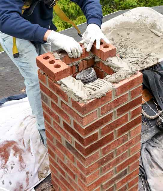 Masonry Repairs: Man installing new bricks and mortar on a chimney.